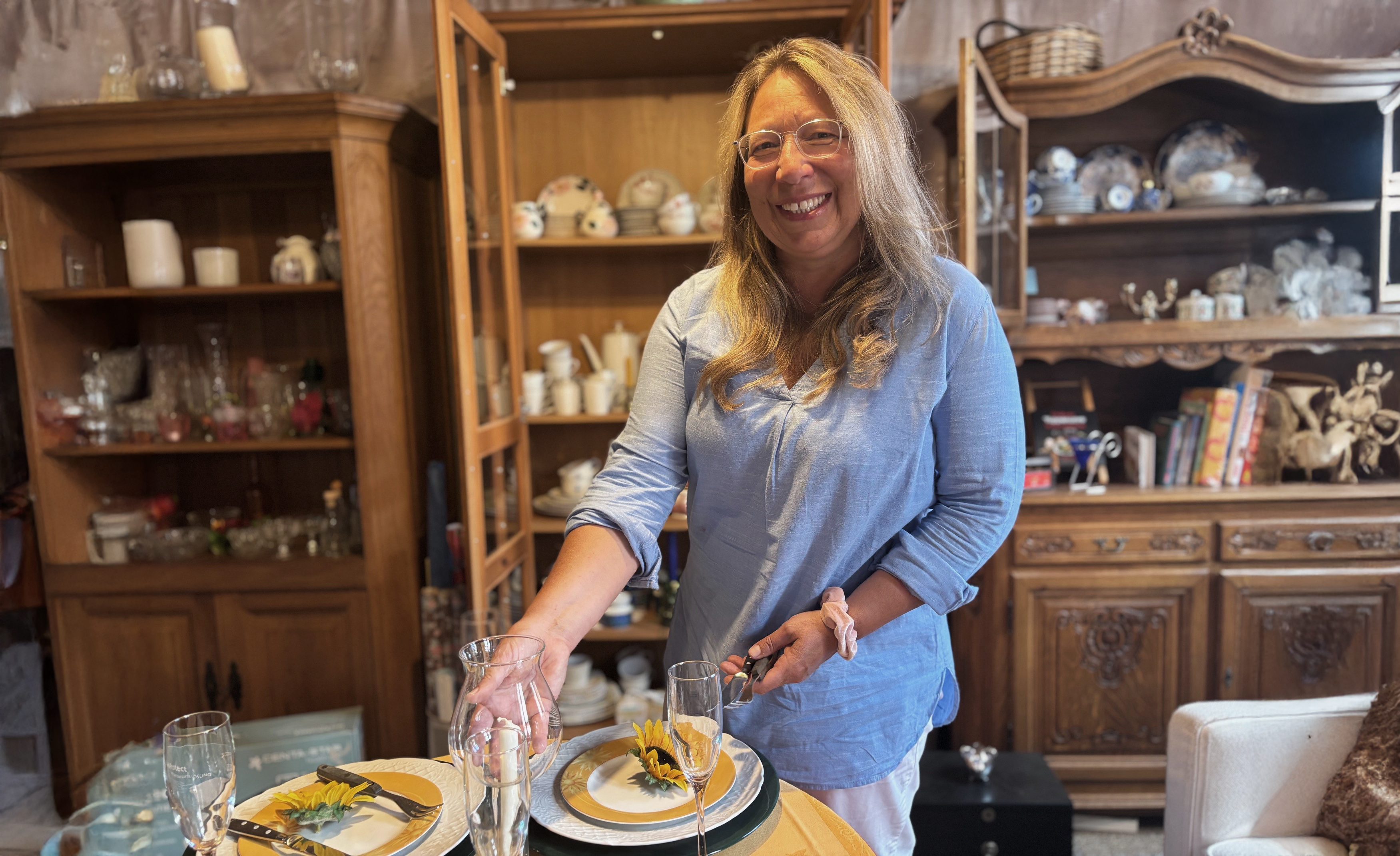 Sabine Frömel steht lächend im Sachensucherladen. Im Hintergrund sieht man Schränke mit Geschirr.