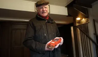 Älterer Herr hat ein rotes Modellauto in der Hand und lächelt in die Kamera.