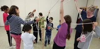 Eine Gruppe Kinder und ihre Betreuerin beim Spielen. Sie bauen einen Turm aus Seilen und Holzklötzen.