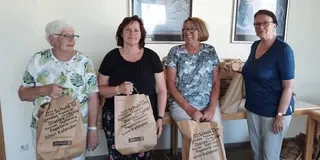 Das Bild zeigt eine Gruppe Frauen, die Tüten, die mit Schulmaterialien gefüllt sind, hochhalten.