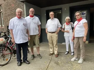 Fünf Personen stehen vor einem Haus und blicken in die Kamera.