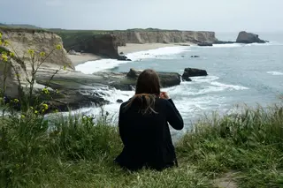 Frau sitzt am Strand und blickt in die Ferne.
