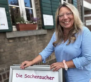 Sabine Frömel steht lachend vor einem Haus.