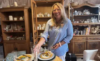Sabine Frömel steht lächend im Sachensucherladen. Im Hintergrund sieht man Schränke mit Geschirr.