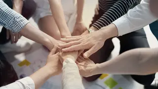 Das Bild zeigt mehrere Hände, die in der Mitte des Bildes zusammenkommen.