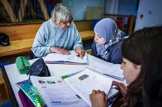 Eine Frau unterstützt ein Mädchen mit Kopftuch bei ihren Hausaufgaben.