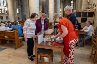 Das Bild zeigt eine Gruppe Menschen in einer Kirche. Sie stehen um einen Tisch und verteilen oder bekommen Essen.