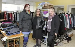 Das Bild zeigt drei Frauen, die in einem Kleiderladen stehen.