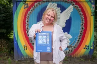 Angelina Eckmann posiert mit ihrer Diakonie-Sammlermappe vor der Zeichnung einer Friedenstaube.